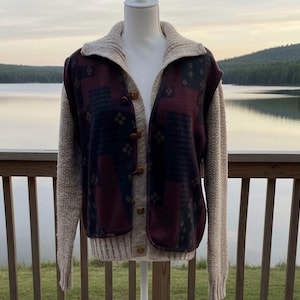 May include: A beige cardigan sweater with a shawl collar and button closure. The front panels feature a geometric pattern in burgundy, navy, and beige. The sleeves are a solid beige knit. The sweater is displayed on a mannequin.
