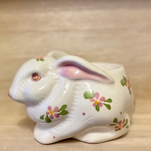 May include: A white ceramic bunny planter with pink ears and green and pink floral details.