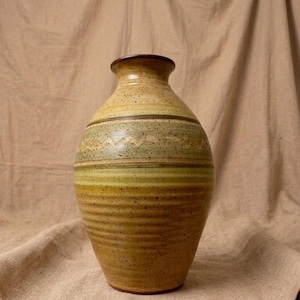 May include: A handmade ceramic vase with a speckled, textured surface. The vase features horizontal bands of color, including shades of yellow, green, and brown. The vase is approximately 12 inches tall and has a narrow neck.