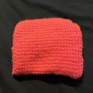 May include: A bright pink crocheted pouch or bag. The pouch is made with a textured stitch and has a soft, fuzzy appearance.