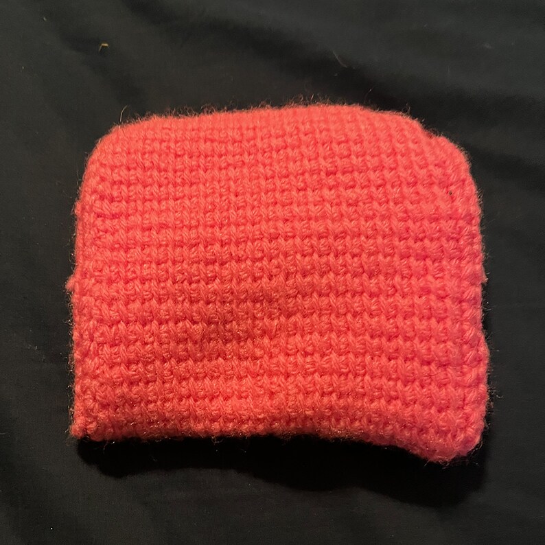 May include: A bright pink crocheted pouch or bag. The pouch is made with a textured stitch and has a soft, fuzzy appearance.