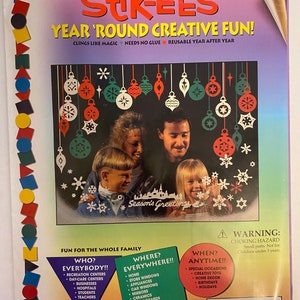 May include: A colorful package of Stik-Ees reusable window clings featuring a winter holiday theme. The package shows a family decorating a window with snowflakes and ornaments. The text on the package reads "Stik-Ees Year 'Round Creative Fun!" and "Season's Greetings".
