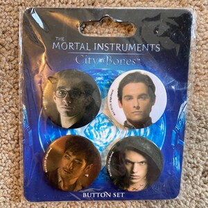 May include: A set of four button pins featuring characters from the book series "The Mortal Instruments: City of Bones". The buttons are round and have a glossy finish. The characters featured are Jace, Simon, Magnus, and Alec.