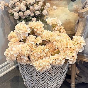 May include: A white wicker basket filled with a bouquet of cream-coloured hydrangeas. The basket is sitting on a dark floor.