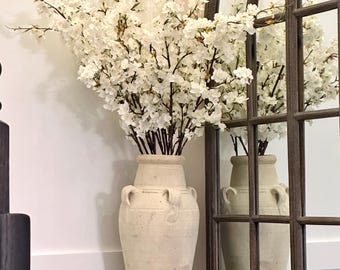 May include: A white ceramic vase with a textured surface and two handles on each side. The vase is filled with white cherry blossom branches.
