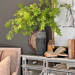 May include: A mirrored cabinet with two drawers and two doors. The cabinet is decorated with a geometric pattern. A vase with green leafy branches sits on top of the cabinet.