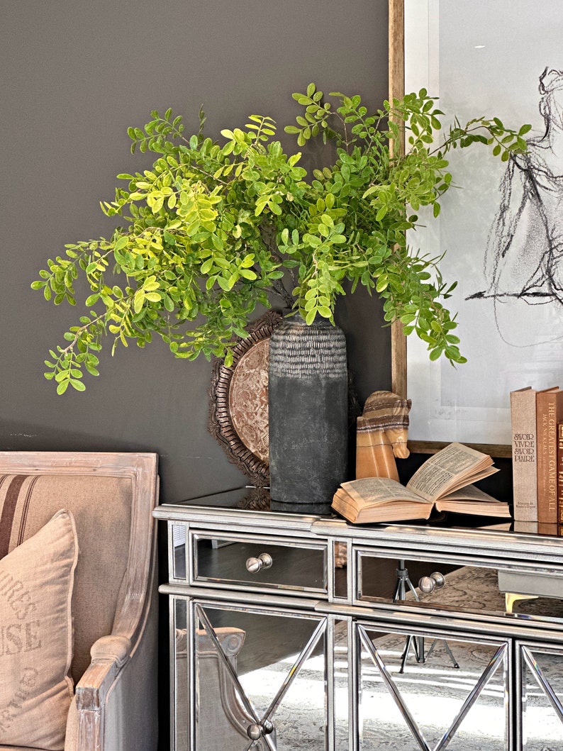 May include: A mirrored cabinet with two drawers and two doors. The cabinet is decorated with a geometric pattern. A vase with green leafy branches sits on top of the cabinet.