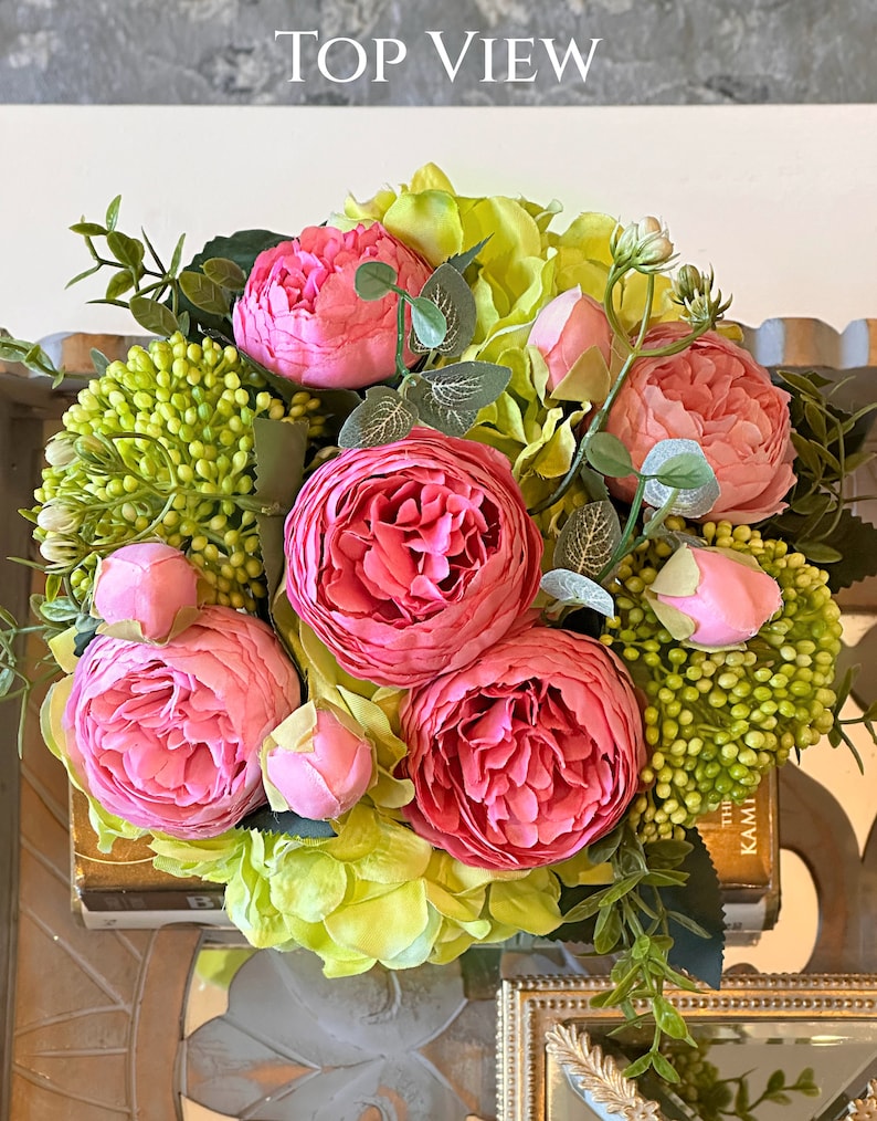 Op de afbeelding: Een boeket van roze pioenen en groene hortensia's in een vaas. De bloemen zijn in een cirkelvormige opstelling gerangschikt en omgeven door groene bladeren.
