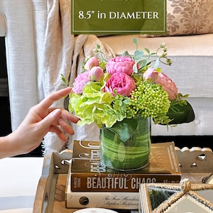 Op de afbeelding: Een glazen vaas met een groen-wit gestreept patroon gevuld met roze en groene kunstbloemen. De vaas is 23 cm hoog en 21,5 cm in diameter. De vaas staat op een stapel boeken met de titel "Beautiful Chaos".