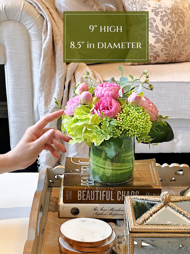 Op de afbeelding: Een glazen vaas met een groen-wit gestreept patroon gevuld met roze en groene kunstbloemen. De vaas is 23 cm hoog en 21,5 cm in diameter. De vaas staat op een stapel boeken met de titel "Beautiful Chaos".