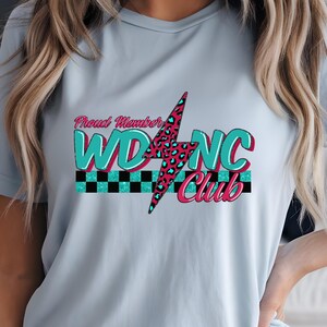 May include: Light blue t-shirt with a graphic design. The design features the text "Proud Member" above "WD NC Club" in teal and pink, with a lightning bolt and a checkered pattern.