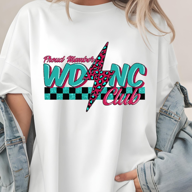 May include: White t-shirt with a graphic design featuring the text "Proud Member WDNC Club". The design includes a lightning bolt with a leopard print pattern, teal and pink lettering, and a checkered stripe.