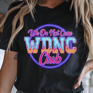 May include: Black t-shirt with a colorful graphic. The graphic features the text "We Do Not Care W.D.N.C. Club" in a playful font, with the letters designed to look like ice cream cones. The design is outlined in a neon purple circle.