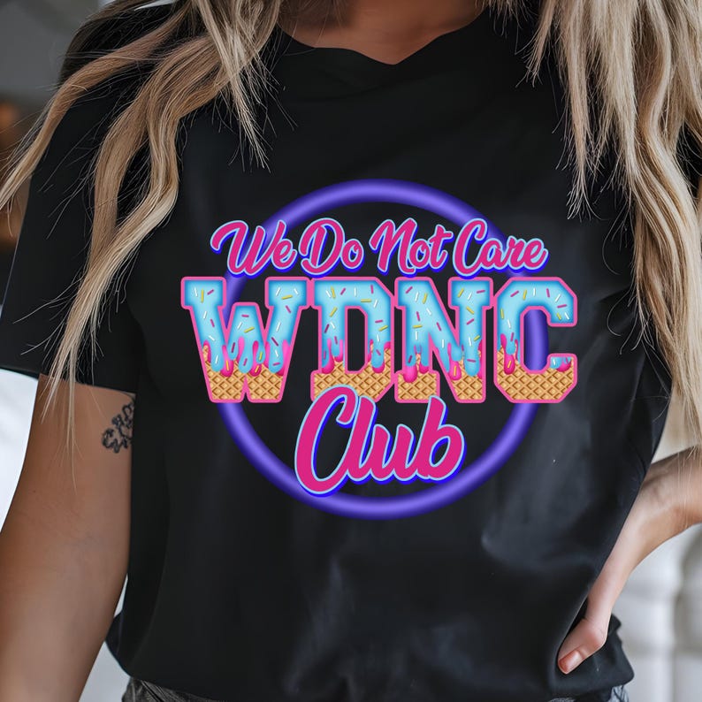 May include: Black t-shirt with a colorful graphic. The graphic features the text "We Do Not Care W.D.N.C. Club" in a playful font, with the letters designed to look like ice cream cones. The design is outlined in a neon purple circle.