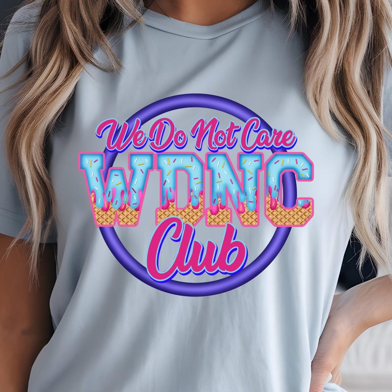 May include: A light blue t-shirt with the text "We Do Not Care WDNC Club" in a colorful, playful design. The text is in a circle with a purple outline, and the letters are decorated with ice cream cone imagery.
