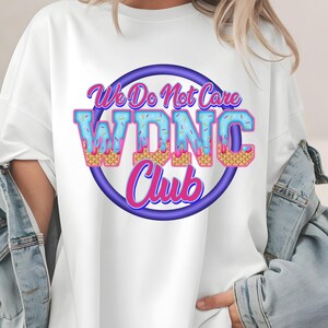 May include: White t-shirt with a colorful graphic. The design features the text "We Do Not Care WDNC Club" in a playful font, with the letters styled to resemble ice cream cones. The text is set within a purple circle.