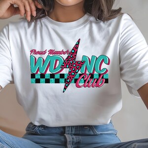 May include: White t-shirt featuring the text "Proud Member WDNC Club". The design includes a pink and teal lightning bolt with a leopard print pattern, teal letters, and a black and white checkered stripe.