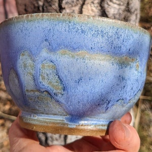 May include: A blue ceramic bowl with a textured glaze. The bowl has a light blue base with darker blue and brown streaks and spots.