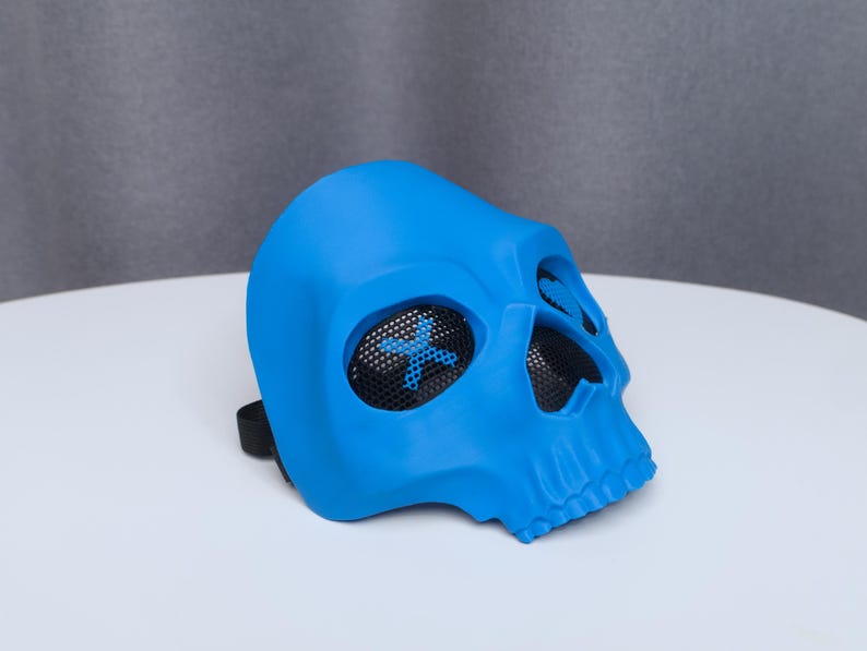May include: A bright blue skull mask with mesh eye coverings and a black strap. The mask is made of a smooth material and has a detailed skull design. The eye coverings have a blue cross design.