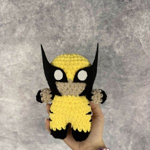 May include: A crocheted yellow and black Wolverine character with a black mask and white eyes.