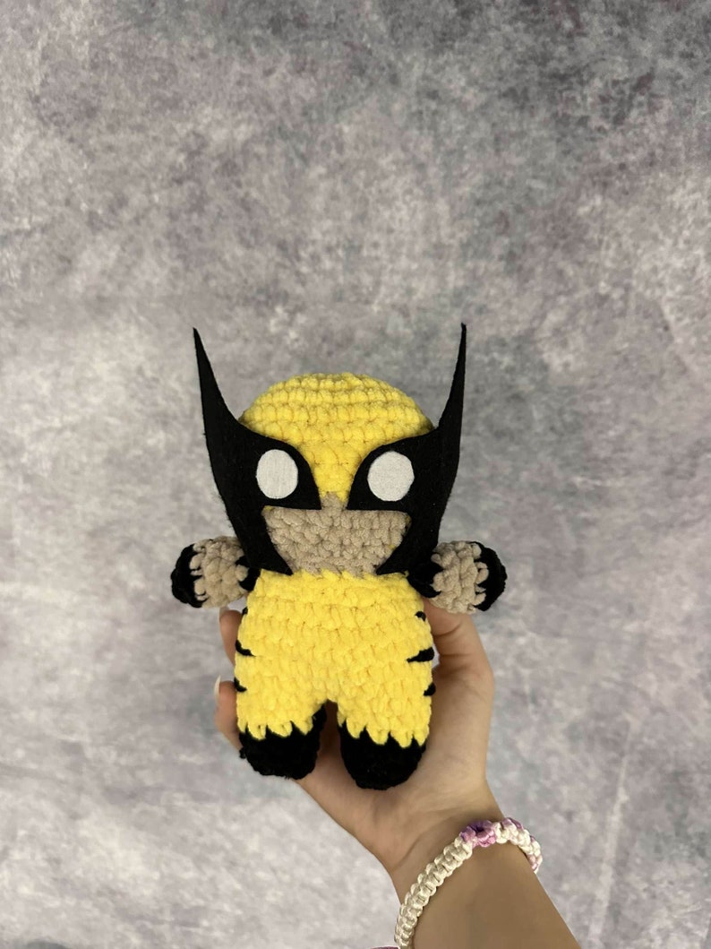 May include: A crocheted yellow and black Wolverine character with a black mask and white eyes.