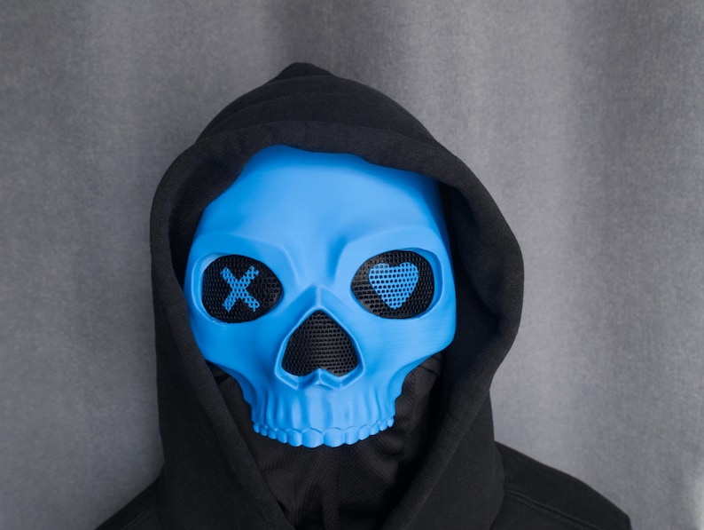 May include: A light blue skull mask with black mesh eye coverings and a black hood. The eye coverings have an X and a heart design. The mask is a costume accessory.