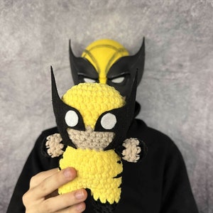 May include: A crocheted yellow and black Wolverine character toy. The toy has a black mask with white eyes and a yellow body with black claws.
