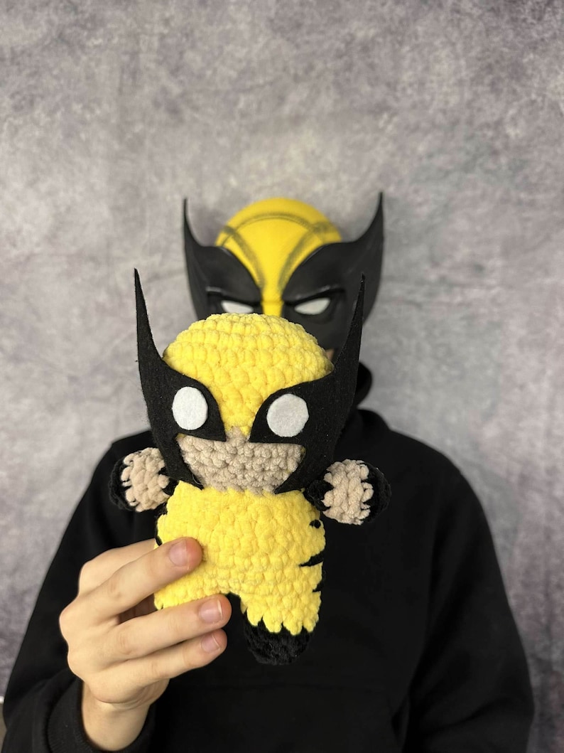 May include: A crocheted yellow and black Wolverine character toy. The toy has a black mask with white eyes and a yellow body with black claws.