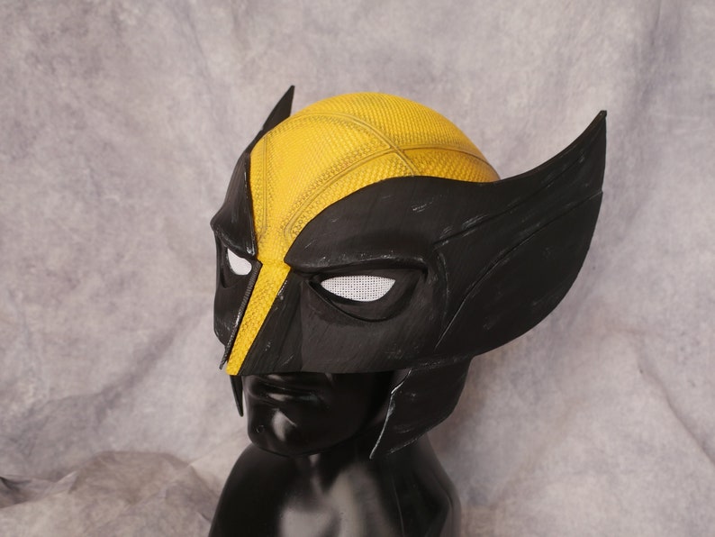 May include: A black and yellow plastic Wolverine mask with a textured surface. The mask has a black and white eye mesh and a black and yellow design.