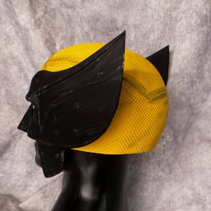 May include: A yellow and black plastic costume mask with a textured surface. The mask is designed to look like a superhero's helmet.