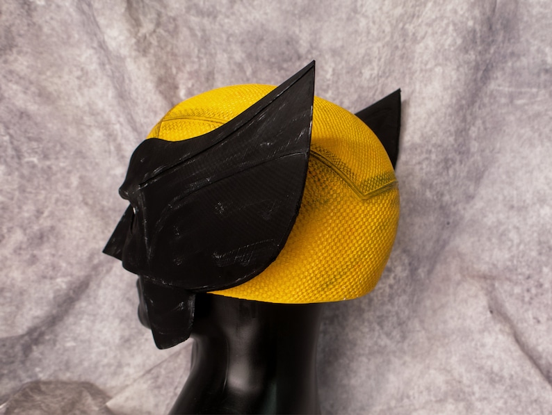 May include: A yellow and black plastic costume mask with a textured surface. The mask is designed to look like a superhero's helmet.
