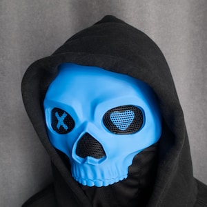 May include: A blue skull mask with mesh eye coverings and a black hood. The eye sockets have an X design. The mask is a vibrant blue color and is set against a gray background.