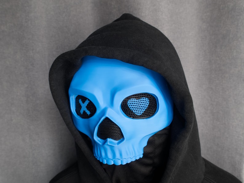 May include: A blue skull mask with mesh eye coverings and a black hood. The eye sockets have an X design. The mask is a vibrant blue color and is set against a gray background.