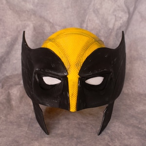 May include: A black and yellow plastic mask with a textured surface. The mask has two eye holes and a pointed chin.