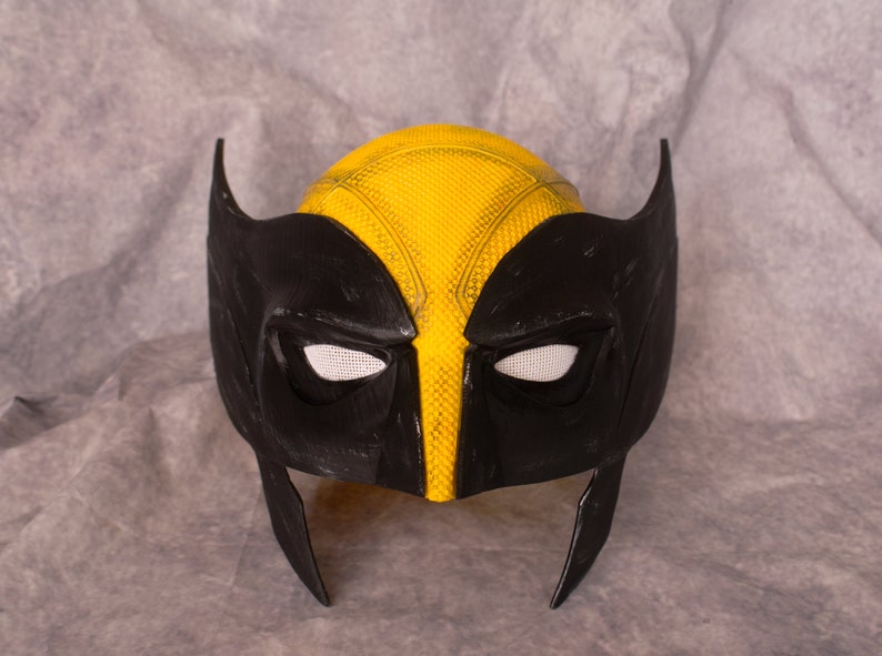 May include: A black and yellow plastic mask with a textured surface. The mask has two eye holes and a pointed chin.