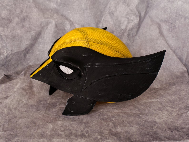 May include: A black and yellow plastic mask with a textured surface. The mask has a single eye opening and a pointed chin.
