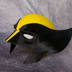 May include: A black and yellow 3D printed helmet with a visor. The helmet is designed to look like a superhero's mask.
