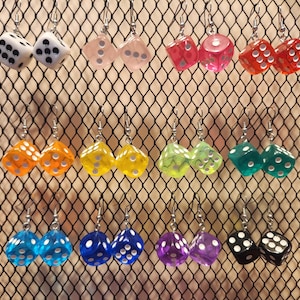 May include: A collection of dice-shaped earrings in various colors, including white, pink, red, orange, yellow, green, teal, blue, purple, and black. Each earring features a pair of dice with white dots, hanging from silver hooks.
