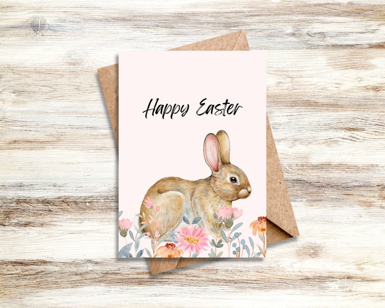 May include: A white card with the text "Happy Easter" in black lettering. A watercolor illustration of a brown rabbit with pink ears surrounded by pink and blue flowers.