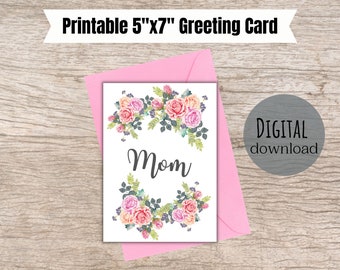 Peut inclure: Carte de vœux imprimable de 12,7 cm x 17,8 cm avec un motif floral et le mot "Maman" au centre. La carte est blanche avec une enveloppe rose.