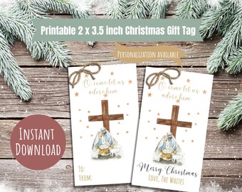 May include: Printable 2 x 3.5 inch Christmas gift tag featuring a watercolor illustration of the nativity scene with a wooden cross and gold stars. The text reads "O come let us adore him" and "Merry Christmas, Love, The Whites".