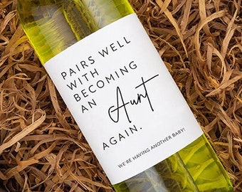 May include: A bottle of white wine with a label that reads "Pairs well with becoming an Aunt again. We're having another baby!"