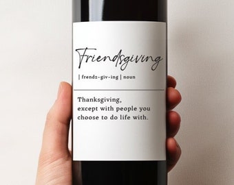 May include: A dark wine bottle with a white label featuring the word "Friendsgiving" in a script font. The label also includes a definition and the phrase "Thanksgiving, except with people you choose to do life with."