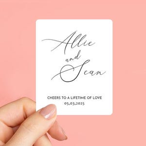 K&ouml;nnte beinhalten: Wei&szlig;e Karte mit schwarzer Kalligraphie, die "Allie und Sean" lautet, mit dem Text "Cheers to a lifetime of love 05,03,2025" darunter.