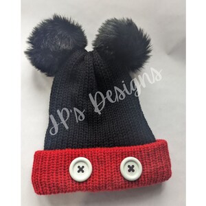 May include: Black knit beanie with red trim and two black pom poms on top. The beanie has two white buttons on the red trim.