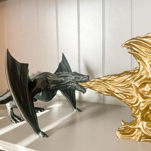 May include: A black dragon figurine with wings outstretched, breathing fire at a gold dragon figurine. The gold dragon is a bookend with a flame design.