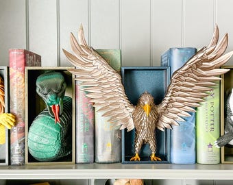 May include: A bookshelf with Harry Potter books and bookends featuring a lion, a snake, a phoenix, and a badger. The bookends are made of a gold-colored metal.