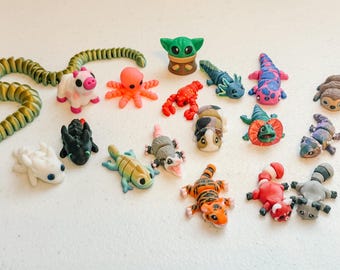 May include: A collection of 17 small, colorful, hand-painted figurines of various animals, including a snake, an octopus, a pig, a sloth, a tiger, a dragon, a lizard, and a frog. The figurines are made of polymer clay and are approximately 2-3 inches tall.