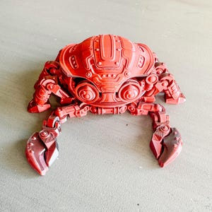 May include: A red, articulated, mechanical crab figurine with a detailed, segmented body and jointed legs. The crab has a textured, metallic finish.