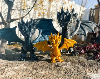 May include: Three dragon figurines, two are black with wings and one is gold with wings. The dragons are posed on a rock surface.